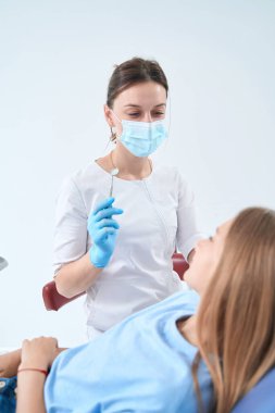 Pediatric dentist holding mouth mirror and looking at patient lying in chair in her office