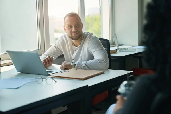 Smiling Man Communicates Dark Haired Colleague Workplace Table Laptop Folder — Stok fotoğraf