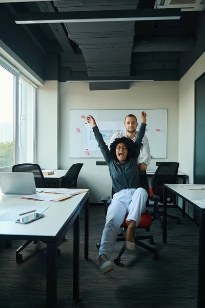 Restrained Young Man Wheeling Cheerful Emotional Multiracial Woman Red Office — Stok fotoğraf