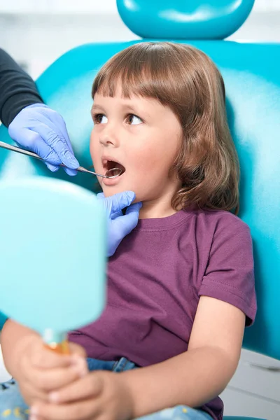 Dental professional in nitrile gloves performing examination of oral cavity of young female patient