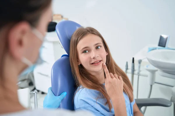 Young lady sitting in dental chair and talking to her pediatric dentist