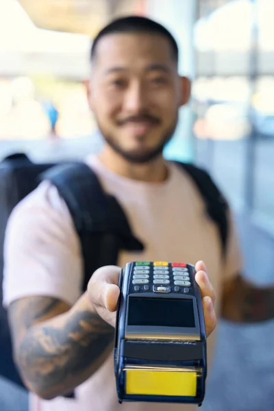 Selective-focus photo of a friendly delivery man extending a hand with terminal and waiting for card swipe