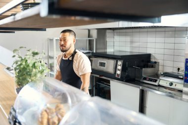 Copy space photo of a focused young man in apron standing in cafe and waiting for customers