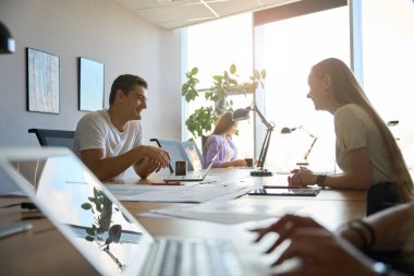 İki kişi daha masalarında çalışırken neşeli bir çalışan bir meslektaşıyla diyalog kuruyor.