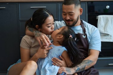 Anne kızını öpüyor, baba ikisine de sarılıyor, Asyalı aile boş zamanlarını utanarak geçiriyor.