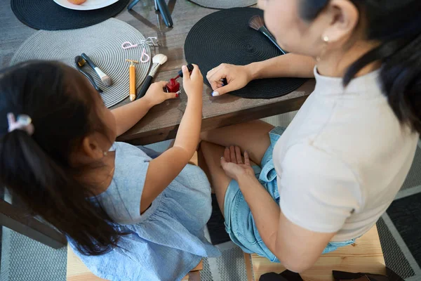图为一名身穿蓝色衣服的女孩和一名亚裔母亲用红色清漆涂指甲的照片 — 图库照片