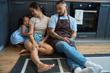 Asyalı ebeveynleri olan tatlı bir kız mutfakta yerde rahatça oturuyor ve annesine sarılıyor.