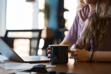 Bir kadın masasında vakit geçirirken, kadın elinde bardakla içki tutuyor.