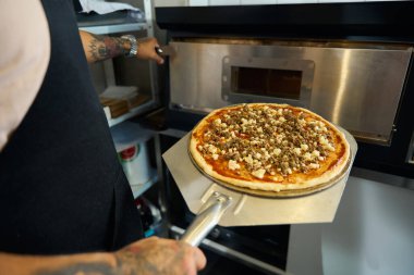 Pişirmeden önce şefin elinde taze yapılmış bir pizzanın küçük bir resmi.
