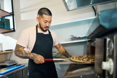 Pizzasını pişirirken fırına dikkatle bakan genç bir adam.