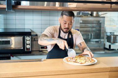 Dikkatli esmer adam pizzayı keserken özel bir bıçakla ona bakıyor.