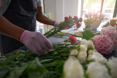 Eldivenli adam masada farklı çiçeklerden bir buket yapar.