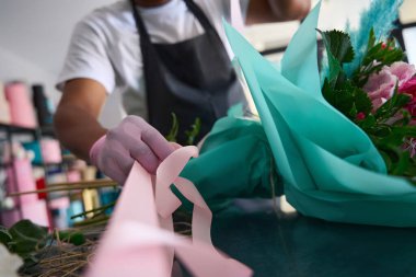 Önlüklü çok ırklı bir adam pembe kurdeleyle çiçek buketini kağıda sarıyordu.