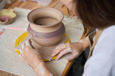 Zanaatkar kadın masaya oturur ve tencerede bir döngü ile çalışır, rahatlatıcı bir dekoratif desen uygular.