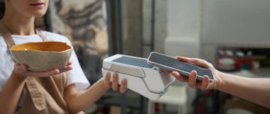 Alıcı telefonu elinde tutuyor ve terminale uyguluyor. Bu da bir kadının elinde.