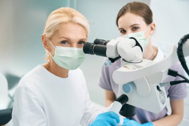 Doktor ve hemşire hastanede mikroskopla modern ofiste poz veriyorlar.