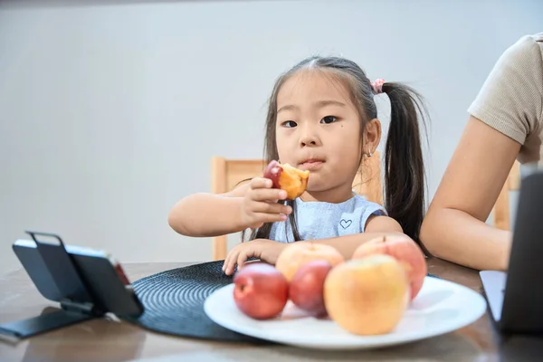Niedliche Asiatische Mädchen Sitzt Vor Telefon Und Isst Einen Pfirsich — Stockfoto