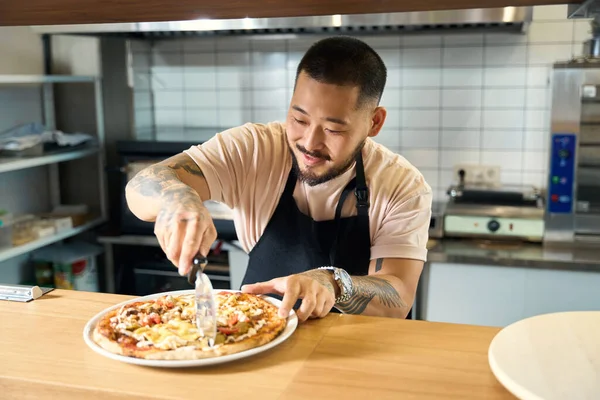 Zevkli şef gülümserken dikkatlice lezzetli pizzayı dilimlere ayırıyor.
