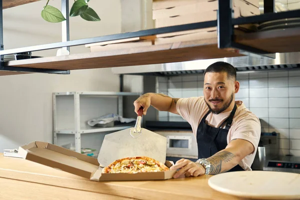 Chef Alegre Olhando Para Câmera Enquanto Cuidadosamente Colocando Uma Pizza — Fotografia de Stock