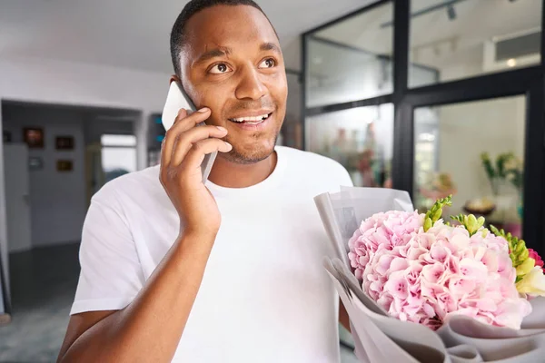 In a flower shop, a man is talking on the phone while holding a bouquet of flowers
