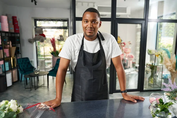 Man in an apron is standing near a table with flowers