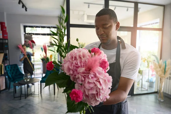 Flower growers in a bright flower shop with large windows hold bouquets