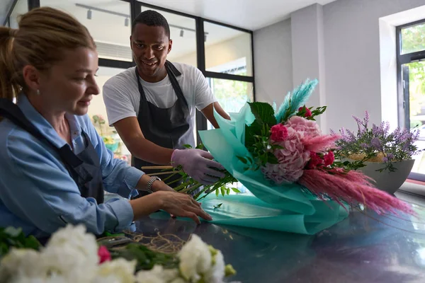 Woman and man wrapping a bouquet in gift paper indoors in a flower shop