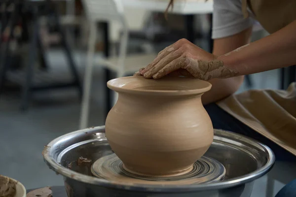 Potter works with a clay vase on a potter wheel, his hands are smeared with clay