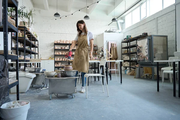 Geniş yaratıcı bir stüdyoda Potter denen kadın çömlekçi çarkında saç kurutma makinesiyle sürahiyi kurutuyor.