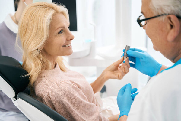 Стоматолог показывает женщине значок и обсуждает хирургию. Концепция здравоохранения и стоматологии