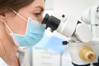 Yetişkin doktor dişçi mikroskop merceğine bakar.