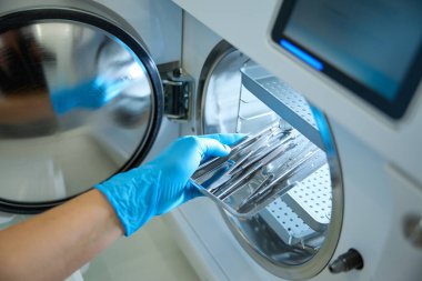Lastik eldivenler, diş aletlerini sterilizatör raflarına koyuyor. Stomatolojik ekipman ve aletler