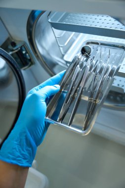 Sterilizasyon için gerekli aletlerin yanında demir kap ve diş aletleri bulunan tıbbi eldivenlerle yakın plan.