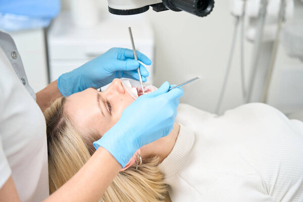 Woman dentist examines the oral cavity of a patient with a special tool