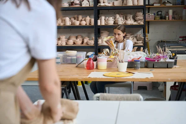 两名妇女在用粘土做的艺术作坊里工作 一名妇女在桌子上涂盘子 另一名妇女则跪在一块粘土上 — 图库照片