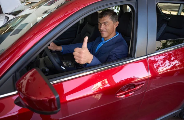 Imponente Hombre Sienta Coche Rojo Muestra Sonríe Alegremente — Foto de Stock