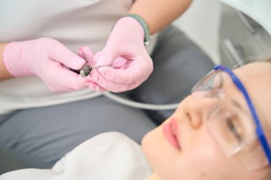 Doktor matkabın içine ince bir matkap yerleştirirken hasta bekliyor.