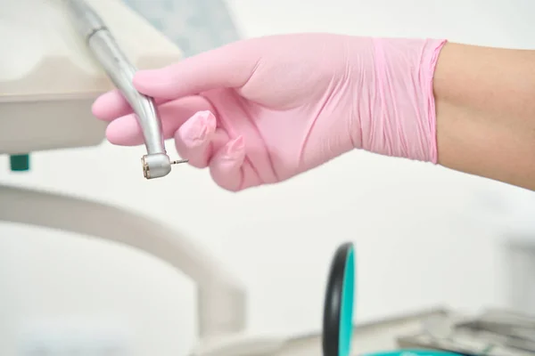 Hand of a caucasian doctor in a pink glove holds a drill