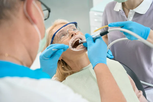 フロントビューポートレートの美しいですエレガントな女性で保護メガネは歯科医院で歯の治療を受けています — ストック写真