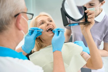 Stomatoloji kliniğinde profesyonel diş tedavisi görürken elinde ayna olan güzel beyaz bir kadının portresini yakından çek.