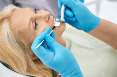 Ecza sandalyesinde uzanan zarif beyaz kadın portresi stomatoloji kliniğinde diş tedavisi görüyor.