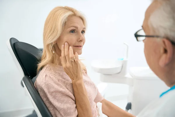 Urocza Biała Kobieta Siedzi Krześle Dentystycznym Podczas Rozmowy Lekarzem Temat — Zdjęcie stockowe
