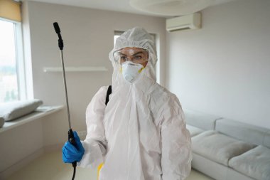 Beyaz üniformalı bir kadın ve dezenfeksiyon aleti tutan solunum cihazı dairede çalışmaya hazır.
