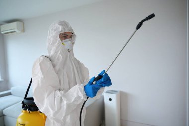 Beyaz üniformalı ve solunum cihazlı bir kadın dezenfeksiyon aleti tutuyor, dairede çalışmaya hazır.