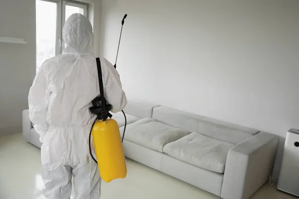 Disinfector from cleaning company in white uniform with yellow sprayer working in the room
