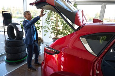 Ciddi bir erkek, yeni bir arabanın bagajını kontrol ediyor. Taşı ve incele