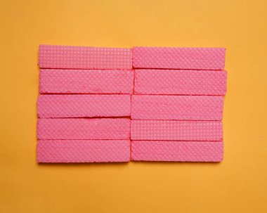 Sarı arka planda düzgünce yerleştirilmiş pembe gofret yığınları. Bir yığın taro aromalı gofret. Lezzetli ve gevrek atıştırmalıklar. Atıştırmalık Renkli gofretler. Yemek fotoğrafçılığı. Lezzetli