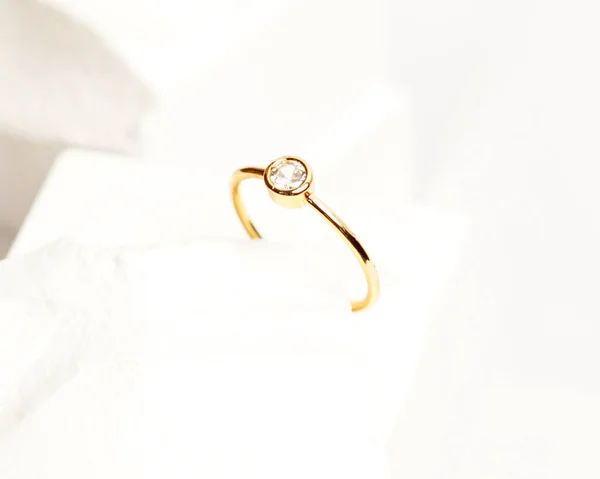 Diamond jewelery ring for social media display. Wedding ring photographed on white stone. Engagement ring with gemstones. Wedding rings isolated on a bright white background, focus blur. Gold ring.