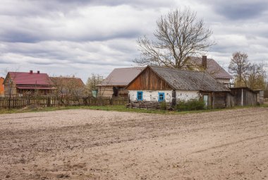 Picturesque rural landscape with a plowed field and an old wooden house beside it. Cloudy day