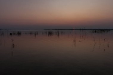 Sunset on the lake. Evening sky with beautiful solar disk is reflected in the water of the lake
